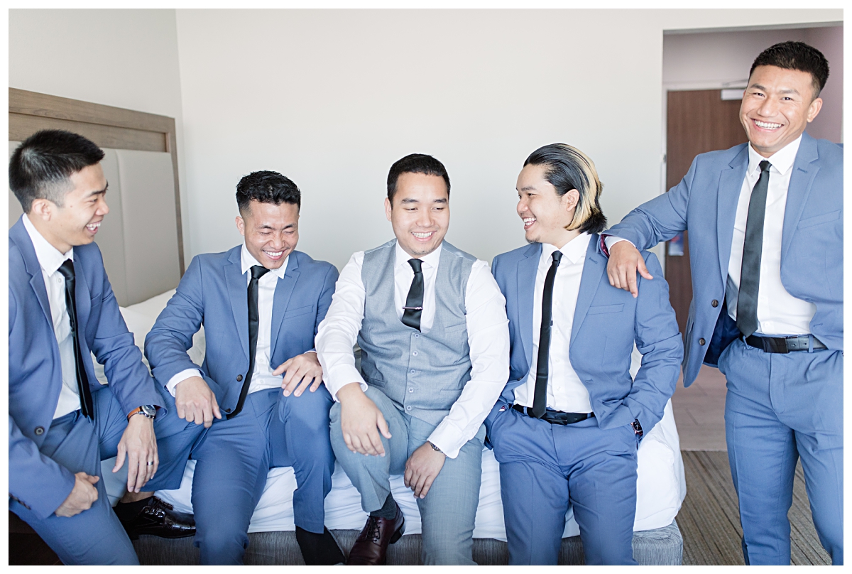 Groomsmen in blue suit laughing with groom during getting ready portion of wedding day photographed by Jenny Bui of Picture Bouquet Studio of a Dallas asian wedding. 