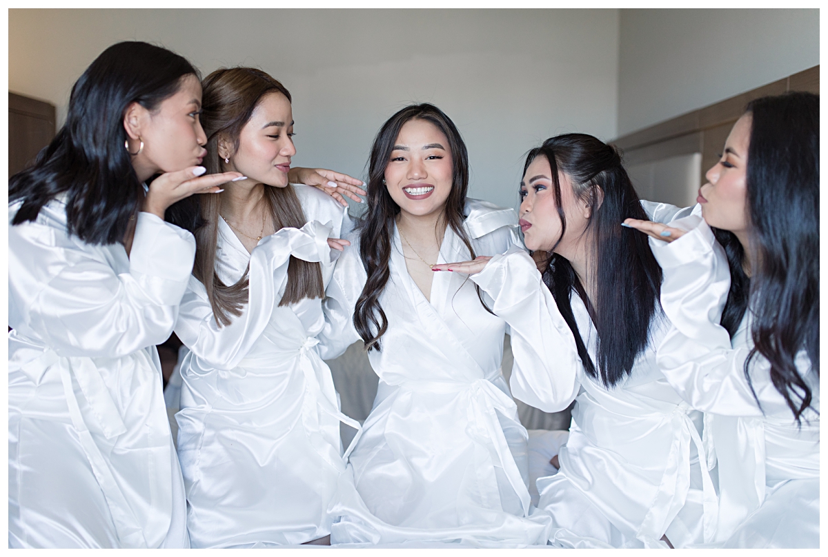 Bridesmaids blowing kisses at bride in their white silk robes during getting ready portion of a Dallas Asian wedding photographed by Jenny Bui of Picture Bouquet Studio. 