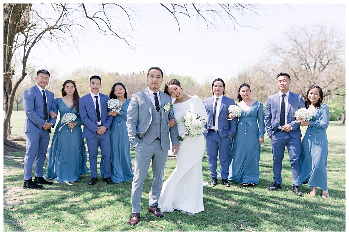 Bridal party in soft blue and cream color palette in background and bride and groom leaning on one another in front from a Dallas Asian wedding photographed by Jenny Bui of Picture Bouquet Studio. 