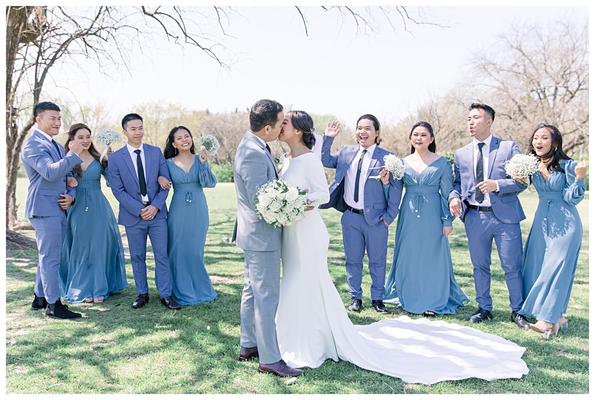 Bride and groom kissing as bridal party cheers in background from a Dallas Asian wedding photographed by Jenny Bui of Picture Bouquet Studio. 