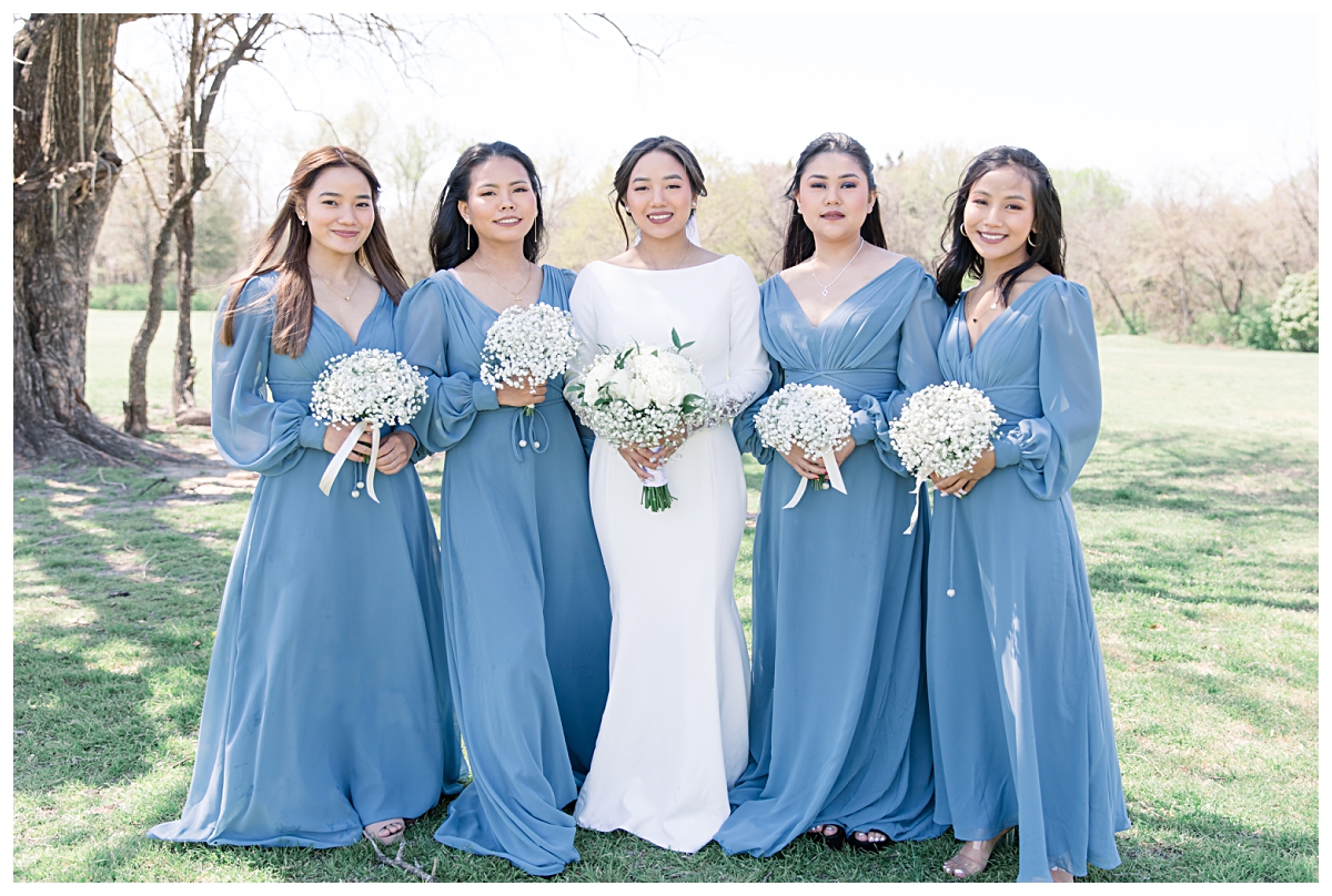 Bridesmaid in soft blue sheer silky long sleeve bridesmaids gown with bride holding bouquets smiling for wedding day portraits photographed by Jenny Bui of Picture Bouquet Studio. 