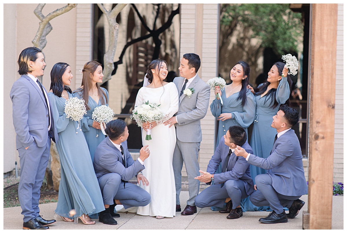 Bridal party in soft blue color palette cheers on bride and groom as they gaze at one another at Highland Oaks Church of Christ during wedding day at Highland Oaks Church of Christ from a Dallas Asian wedding photographed by Jenny Bui of Picture Bouquet Studio. 