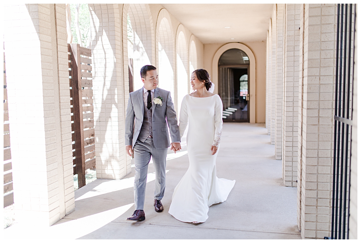 Bride and groom holding hands and walking along walkway at Highland Oaks Church of Christ from a Dallas Asian wedding photographed by Jenny Bui of Picture Bouquet Studio. 