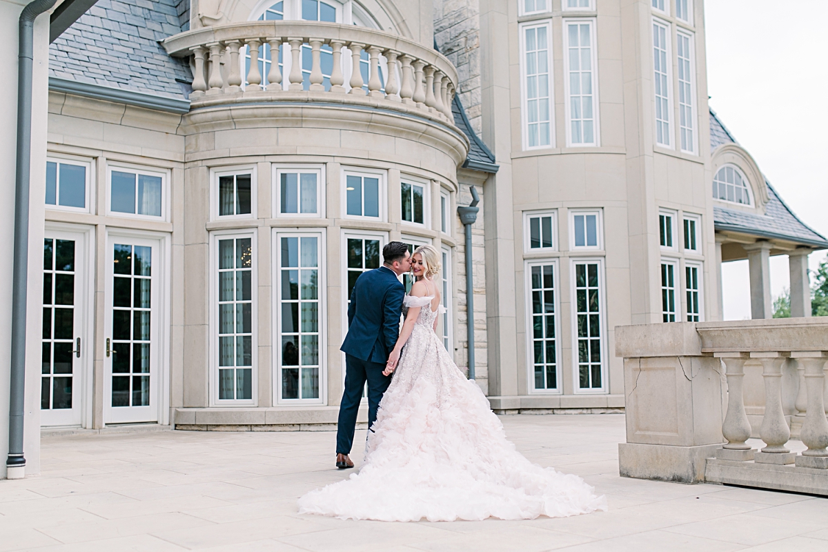 Groom in navy blue suit kisses bride in blush wedding dress at The Olana wedding venue photographed by Dallas Wedding photographer Jenny Bui of Picture Bouquet Studio. 