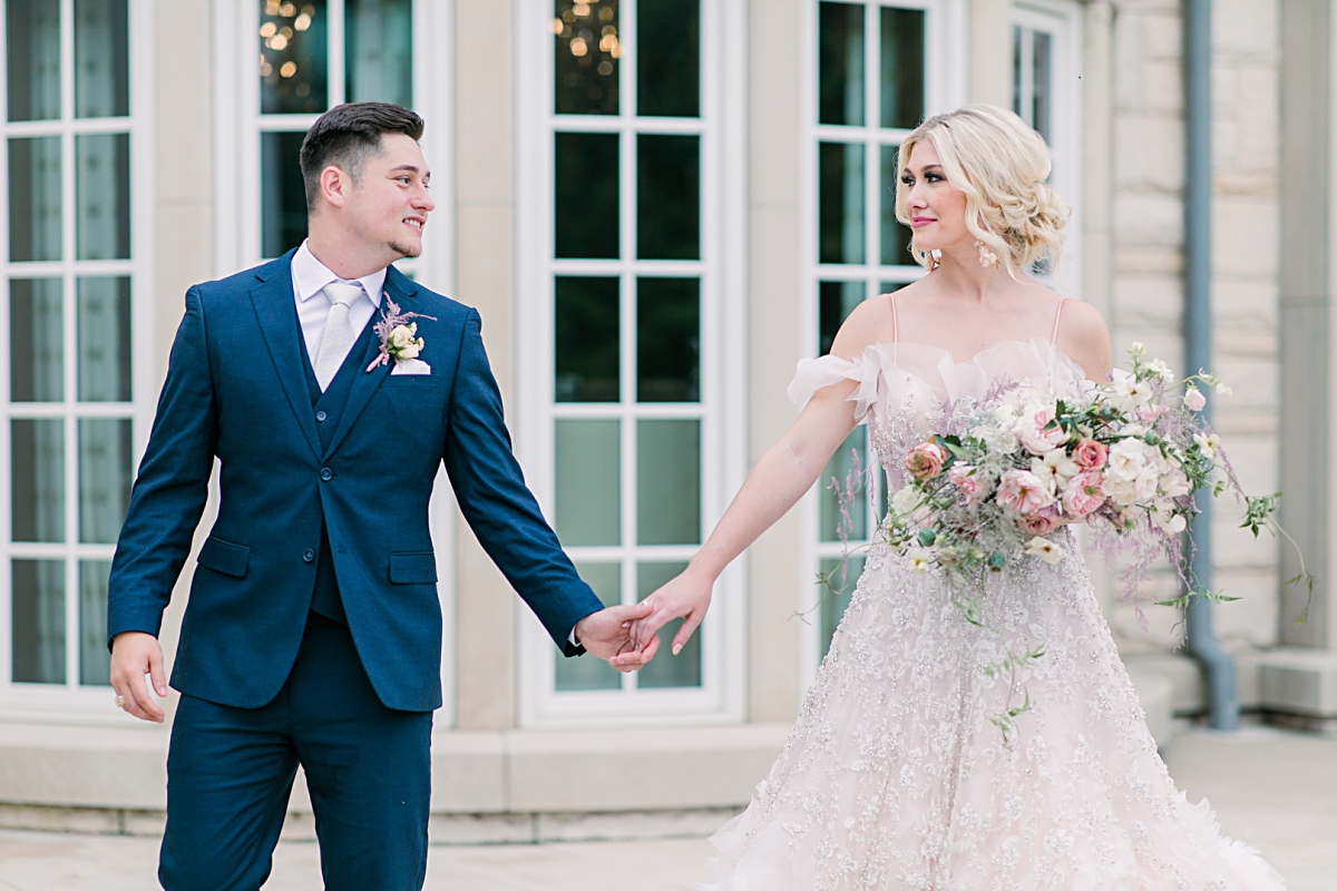 Bride in blush wedding dress holding hands with groom in navy suit at The Olana wedding venue photographed by Dallas Wedding photographer Jenny Bui of Picture Bouquet Studio. 