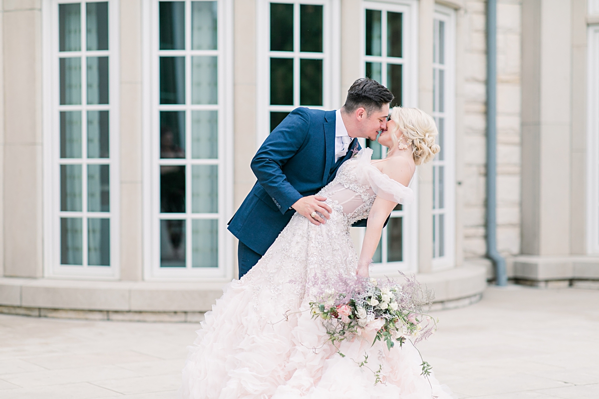 Groom in navy blue suit dipping bride in beautiful blush wedding dress outside the Olana wedding venuephotographed by Dallas Wedding photographer Jenny Bui of Picture Bouquet Studio. 