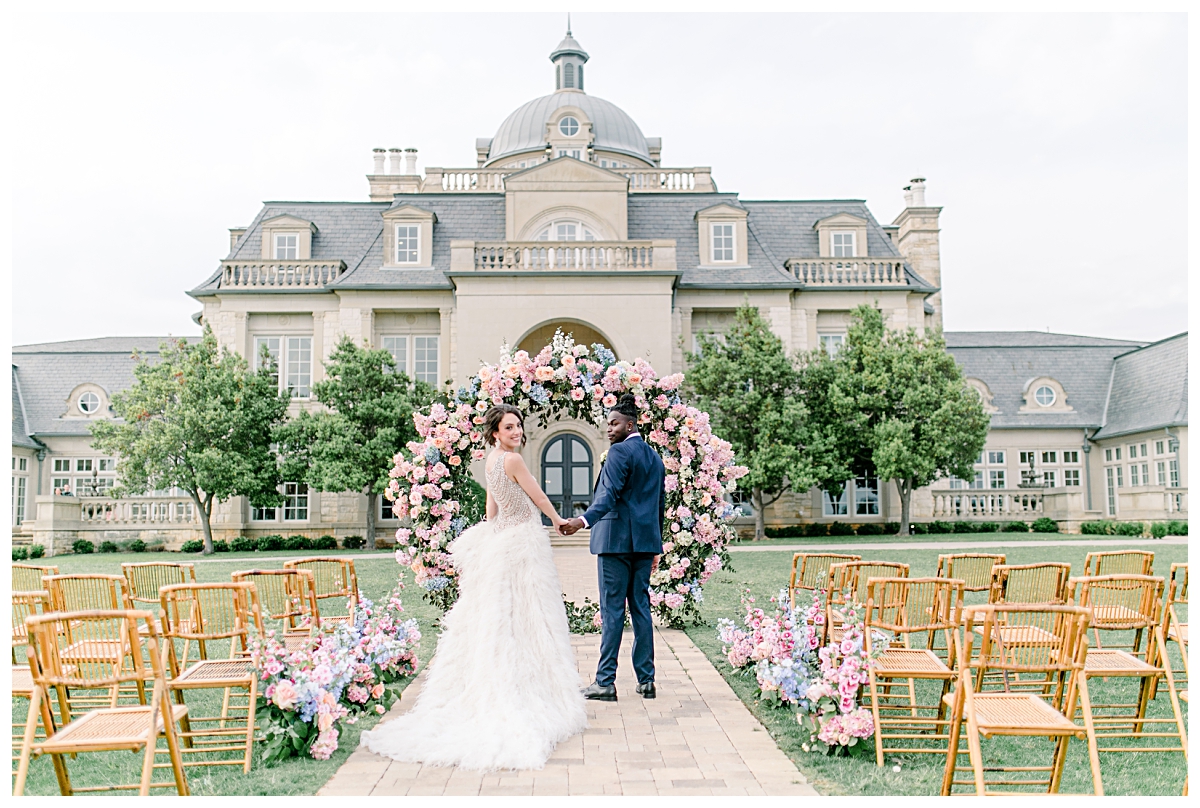 Groom in navy suit leading bride in vintage beaded and feathered gown down aisle as she looks back at The Olana Wedding venue for styled shoot photographed by Dallas Wedding Photographer Jenny Bui of Picture Bouquet Studio. 