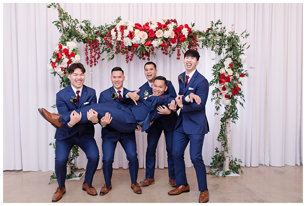 Groomsment holding groom in navy suit up in fun pose at Zander House wedding photographed by Dallas wedding photographer Jenny Bui of Picture Bouquet Studio. 