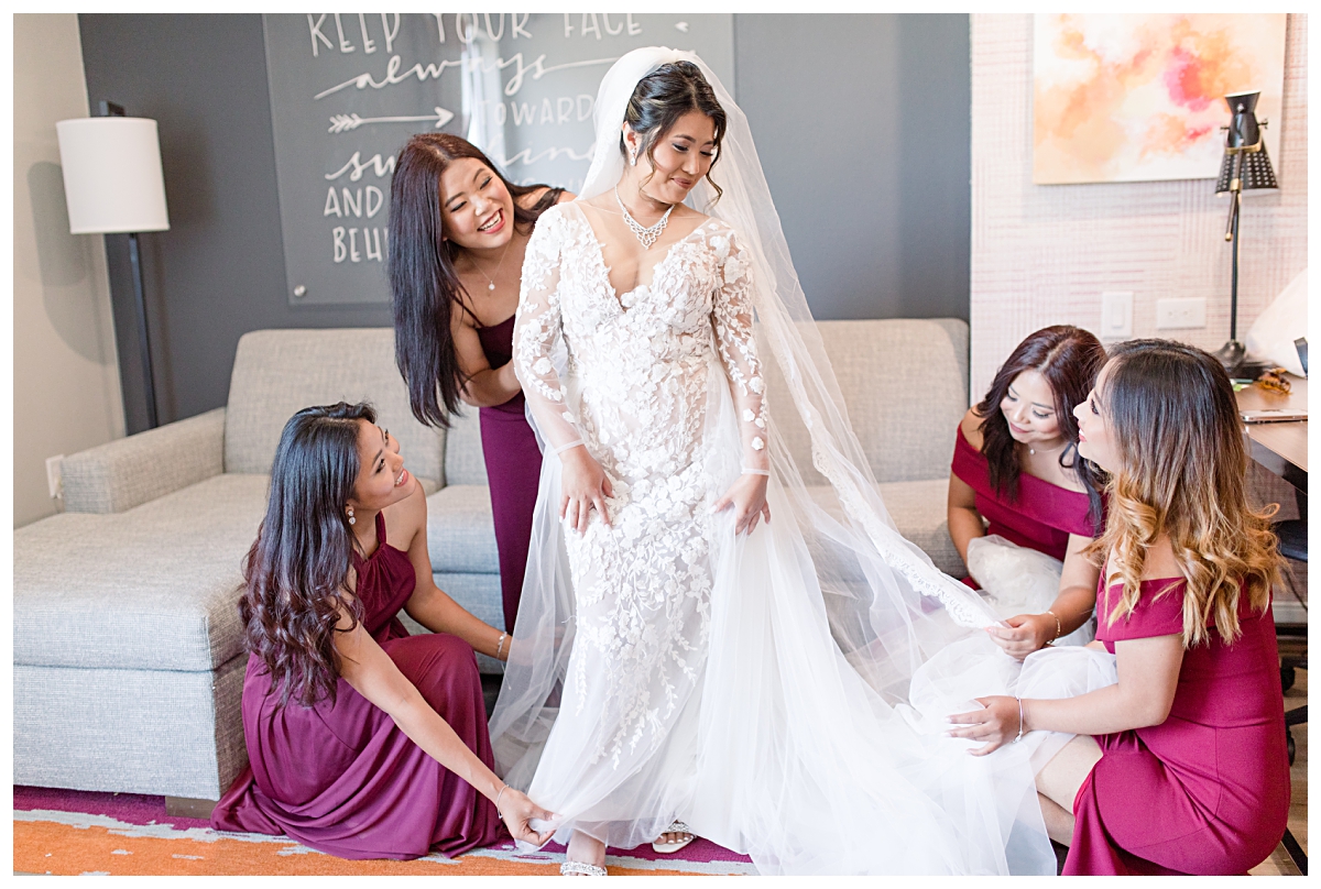 Bridesmaids in burgundy dresses help bride get ready during getting ready portion of wedding day photographed by Dallas wedding photographer Jenny Bui of Picture Bouquet Studio. 