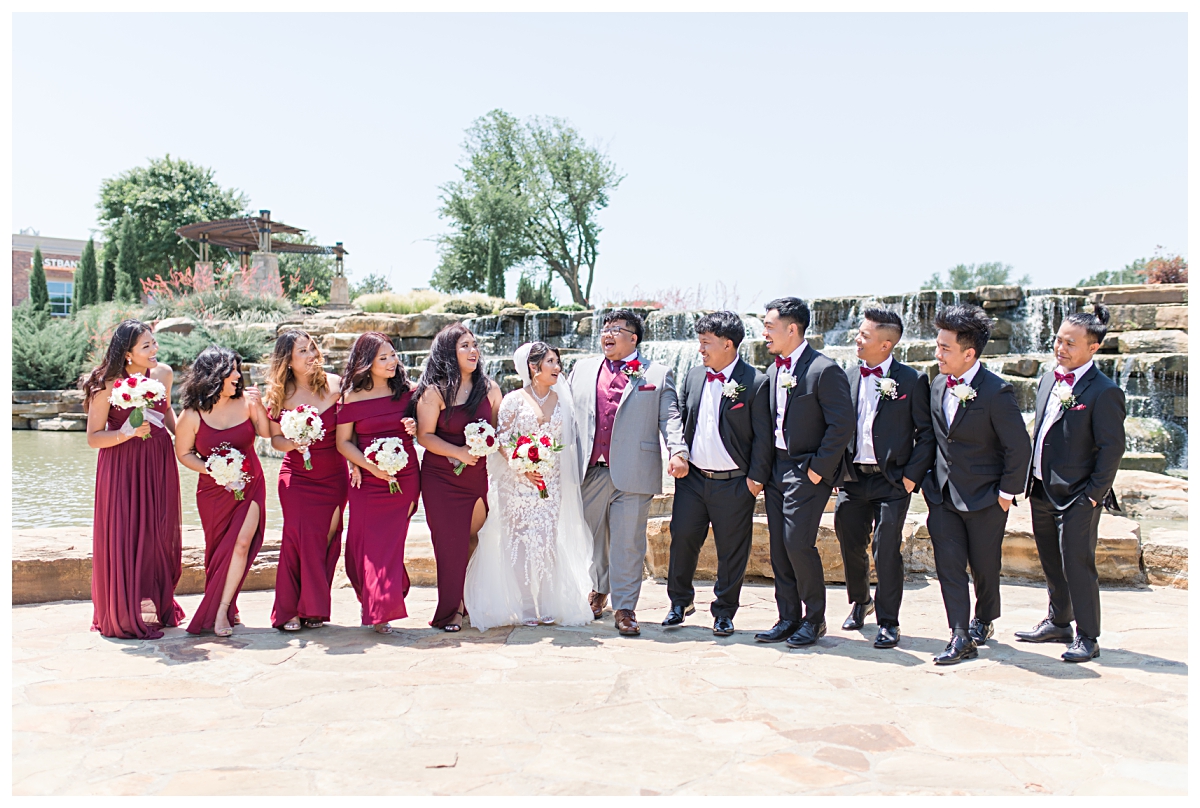 Bridal party in burgundy and cream walking and laughing at Flower Mound River Walk during Lewisville Texas wedding day photographed by Dallas wedding photographer Jenny Bui of Picture Bouquet Studio. 