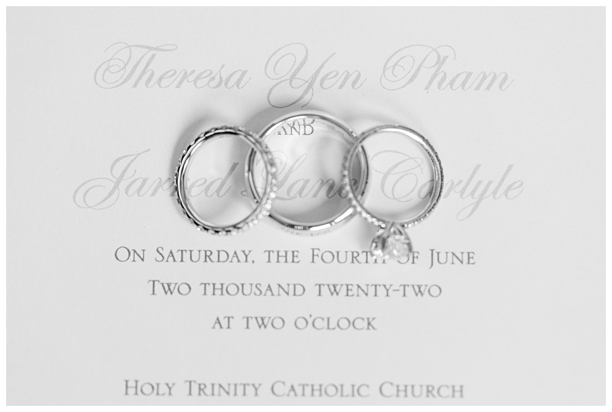 Ring shot of wedding bands and engagement ring on top of wedding day invitation photographed by Dallas wedding photographer Jenny Bui of Picture Bouquet Studio for Holy Trinity Catholic Church wedding in Dallas, TX.  