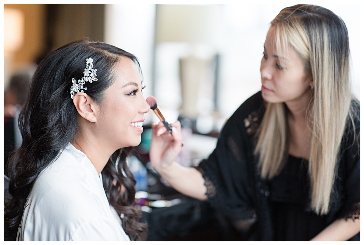 Makeup artist putting finishing touches on bride on wedding day photographed by Dallas wedding photographer Jenny Bui of Picture Bouquet Studio for Holy Trinity Catholic Church wedding in Dallas, TX.  