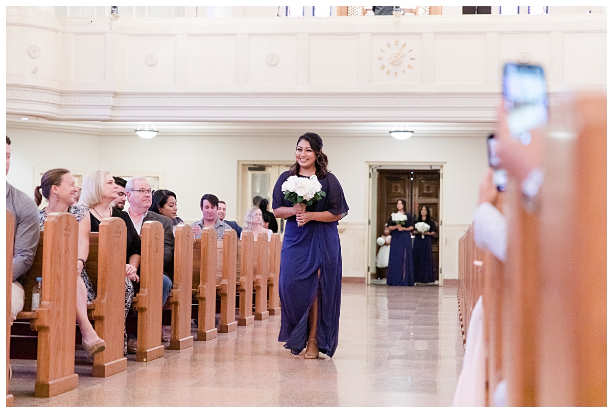 Bridemaid in royal blue dress walking down aisle during processional photographed by Dallas wedding photographer Jenny Bui of Picture Bouquet Studio for Holy Trinity Catholic Church wedding in Dallas, TX.  