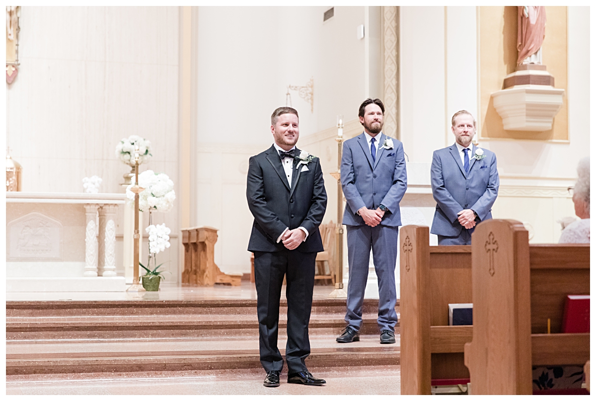 Groom gazing down aisle during processional photographed by Dallas wedding photographer Jenny Bui of Picture Bouquet Studio for Holy Trinity Catholic Church wedding in Dallas, TX.  