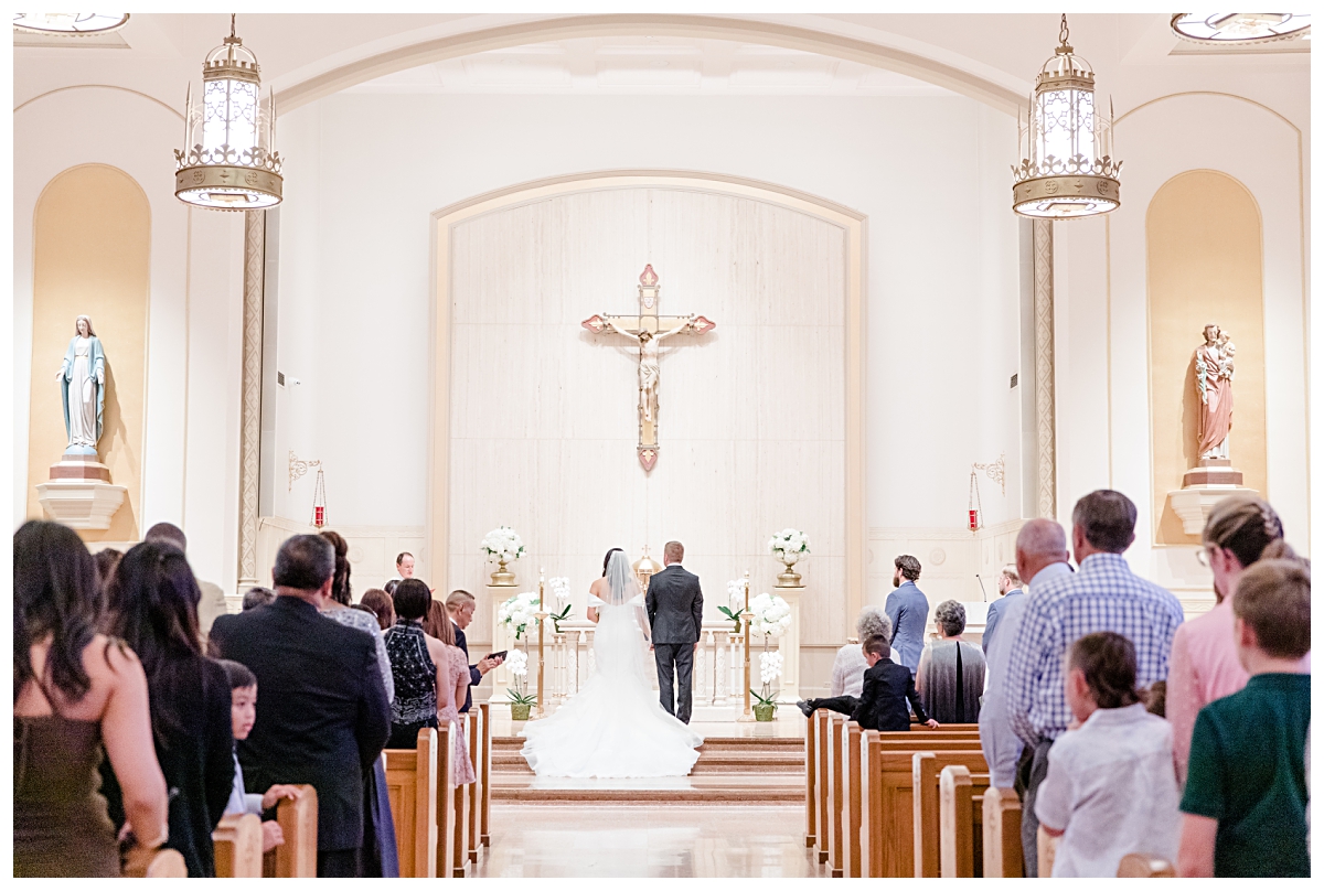 Back view of bride and groom standing on the altar photographed by Dallas wedding photographer Jenny Bui of Picture Bouquet Studio for Holy Trinity Catholic Church wedding in Dallas, TX.  