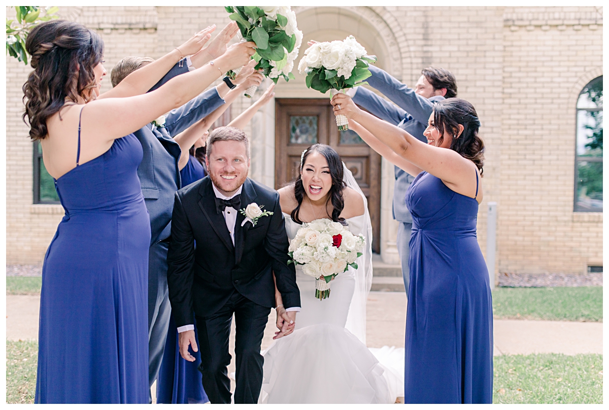 Bride and groom laughing as they walk under tunnel of bridesmaids and groomsmen's arms photographed by Dallas wedding photographer Jenny Bui of Picture Bouquet Studio for Holy Trinity Catholic Church wedding in Dallas, TX.  