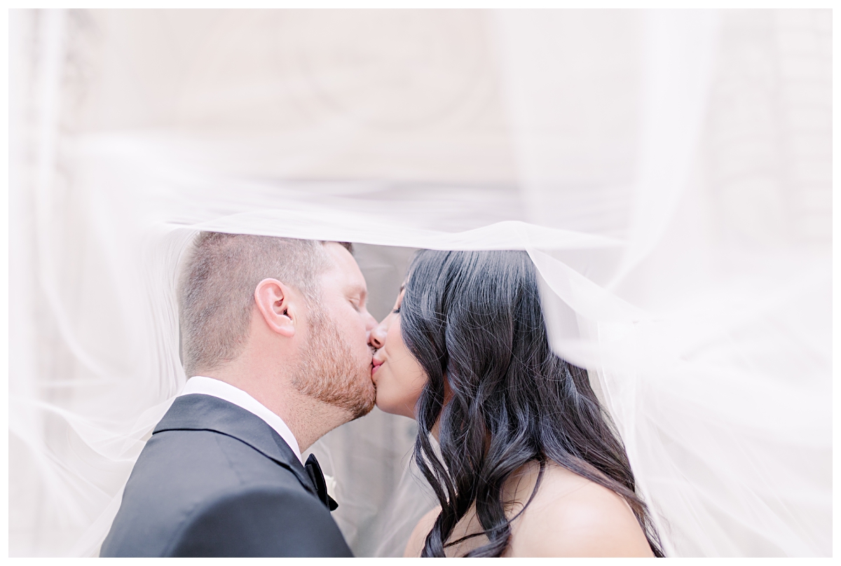 Bride giving groom kisses beneath the veil during wedding day portraits photographed by Dallas wedding photographer Jenny Bui of Picture Bouquet Studio for Holy Trinity Catholic Church wedding in Dallas, TX.  