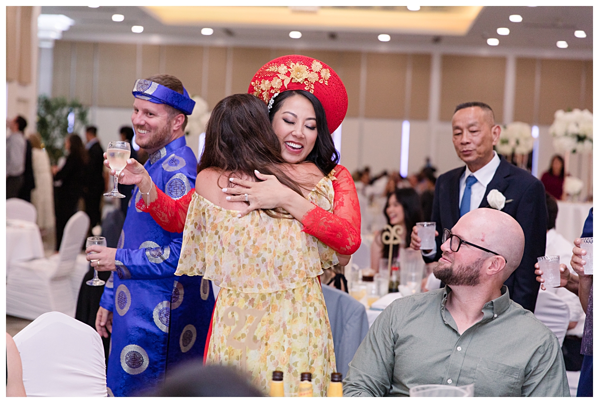 Bride in traditional ao dai hugs guest during table greetings photographed by Dallas wedding photographer Jenny Bui of Picture Bouquet Studio for The Pearl  wedding in Dallas, TX.   
