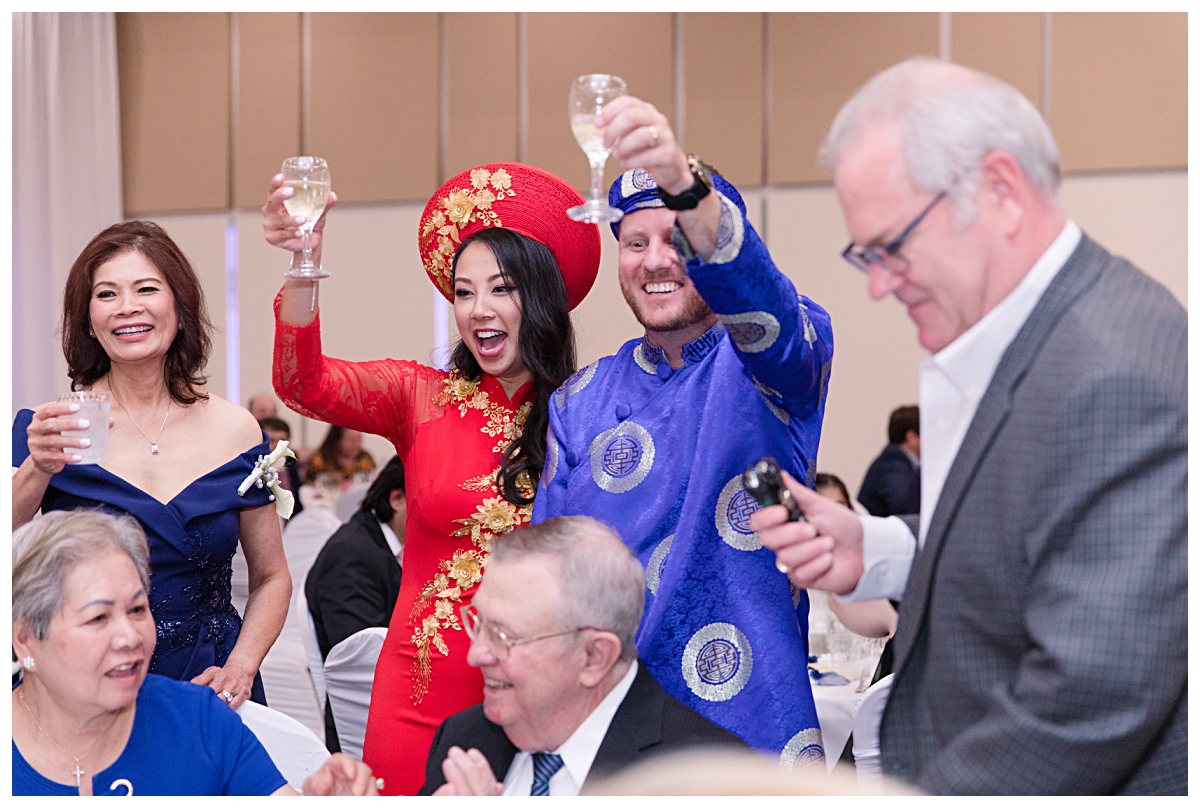 Bride and groom in traditional Vietnamese ao dai cheers with guests during table greetings photographed by Dallas wedding photographer Jenny Bui of Picture Bouquet Studio for The Pearl  wedding in Dallas, TX.   
