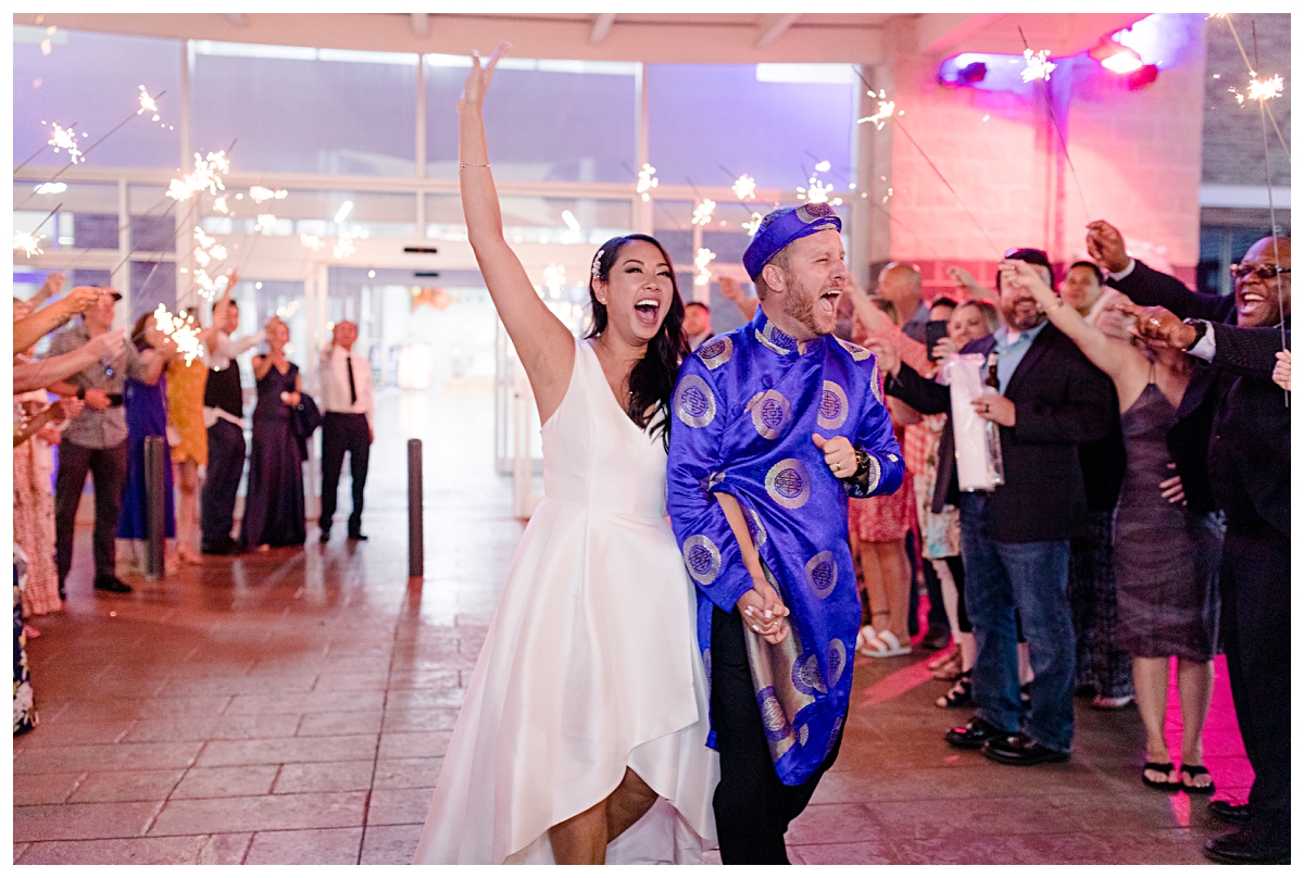 Bride and groom cheering happily as they walk through their sparkler exit at end of reception photographed by Dallas wedding photographer Jenny Bui of Picture Bouquet Studio for The Pearl  wedding in Dallas, TX.   