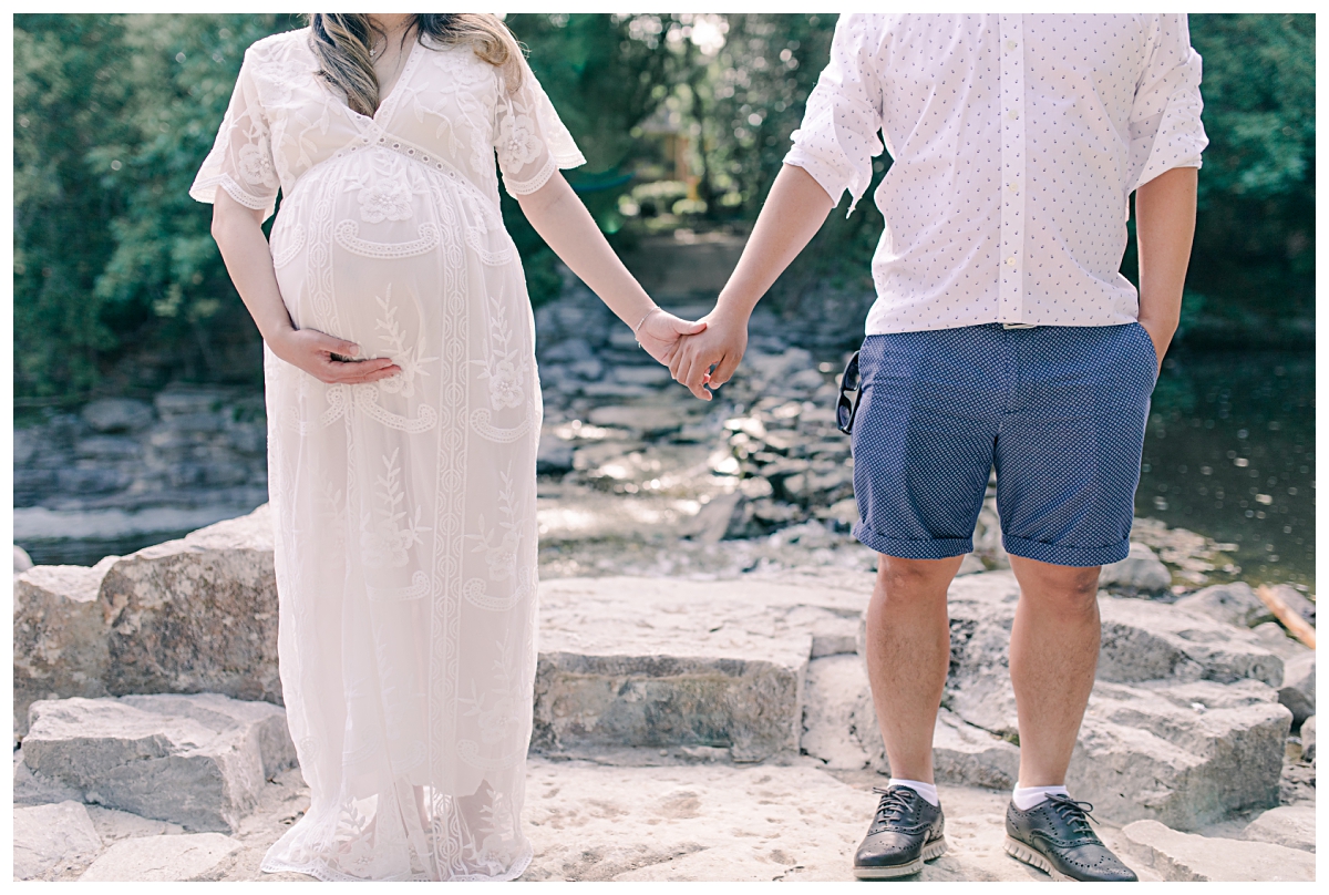 Pregnant woman in cream lace maternity dress holding belly and husband's hand for Prairie Creek Maternity session photographed by Dallas wedding and portrait photographer Jenny Bui of Picture Bouquet Studio. 