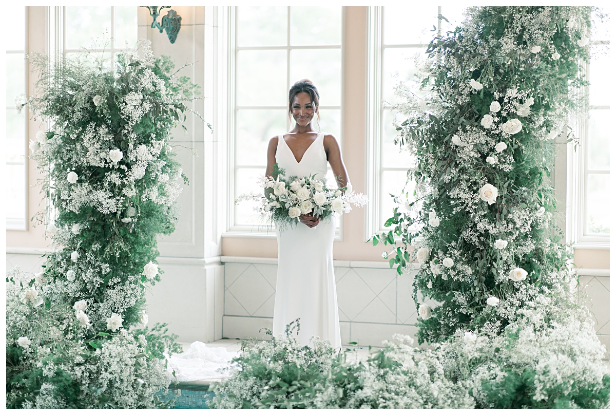 Gorgeous bride smiling at camera in center of beautiful floral arrangement at edge of pool for editorial bridal shoot at The Olana pool room photographed by Dallas wedding photographer Jenny Bui of Picture Bouquet Studio. 