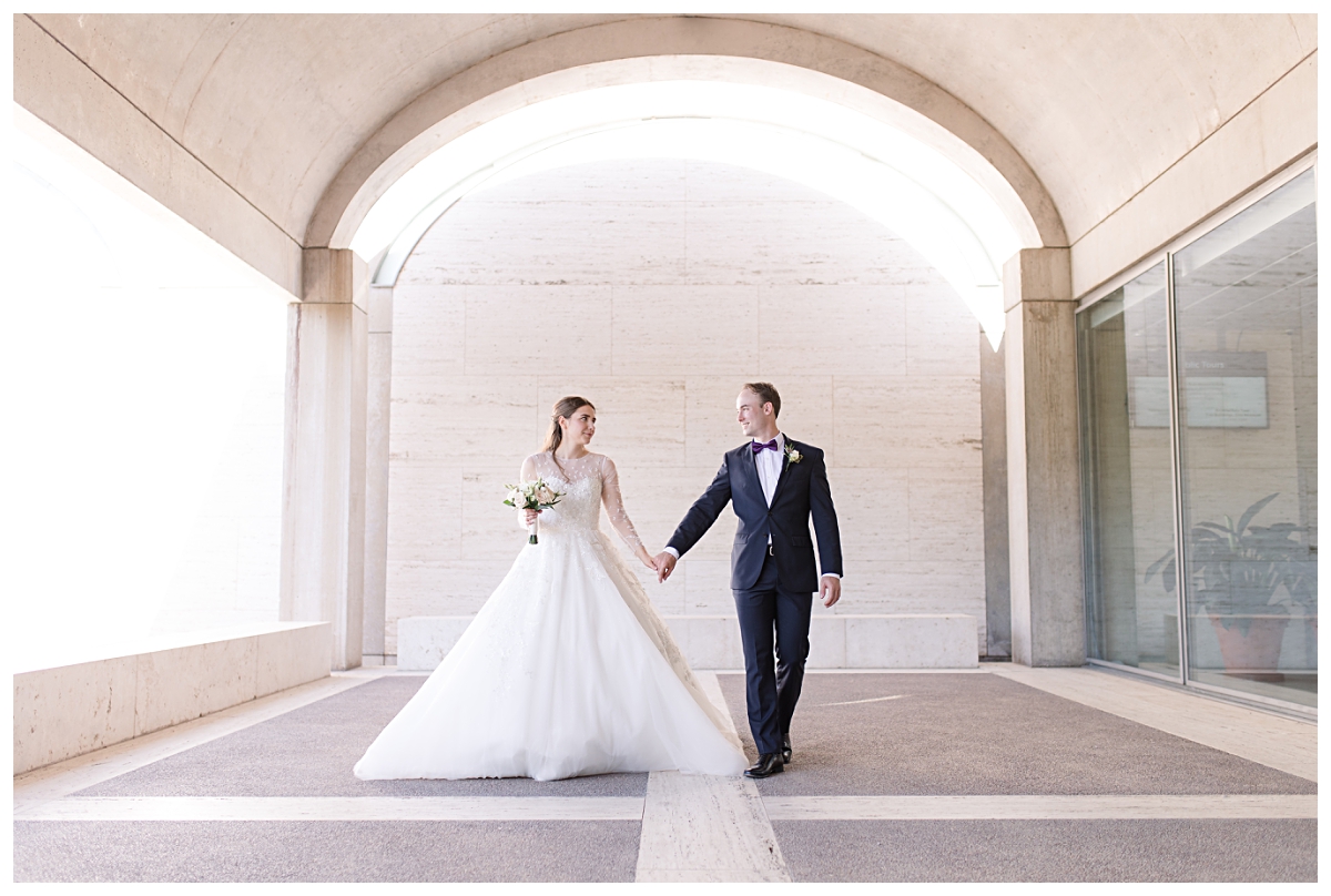 Bride and groom walking underneath archway at Kimbell Arts Musuem photographed by Dallas wedding photographer Jenny Bui of Picture Bouquet Studio.