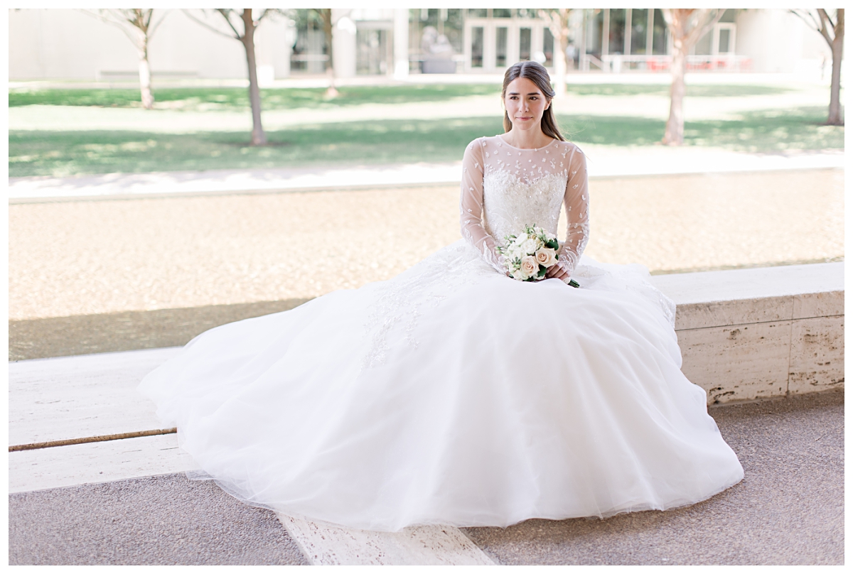 Beautiful bride in long sleeve white lace wedding gown poses sitting for Kimbell Art Museum wedding portraits photographed by Dallas wedding photographer Jenny Bui of Picture Bouquet Studio. 