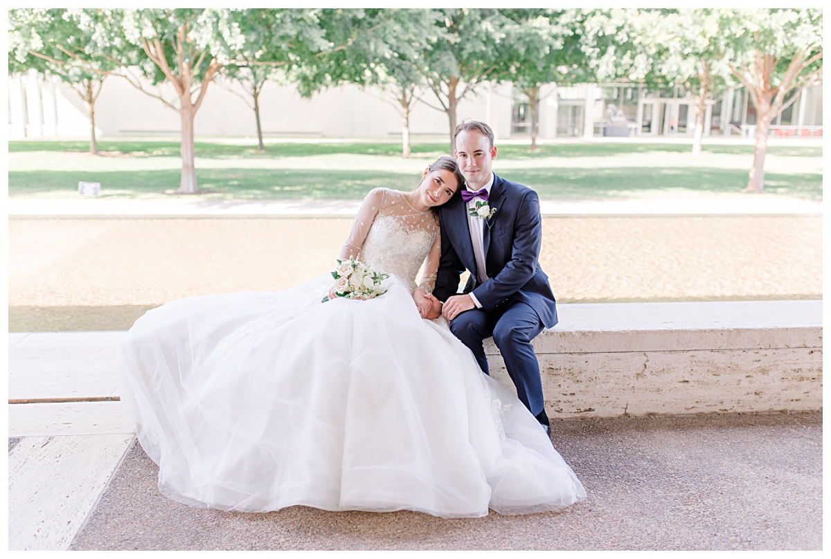 Bride in white lace and beaded wedding dress and groom in navy suit smiles at camera for Kimbell Art Museum wedding portraits photographed by Dallas wedding photographer Jenny Bui of Picture Bouquet Studio. 