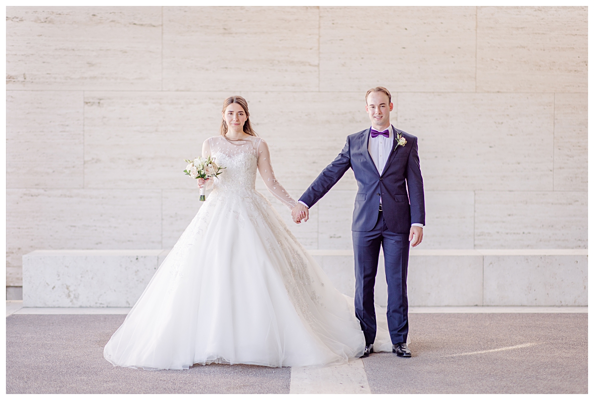 Bride in white long sleeve wedding dress holds hands with groom in navy suit for Kimbell Art Museum wedding portraits photographed by Dallas wedding photographer Jenny Bui of Picture Bouquet Studio. 