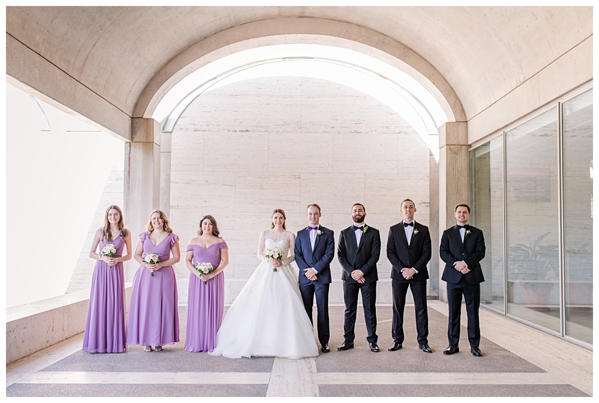 Gorgeous bridesmaid in lilac bridesmaids dresses and groomsmen in black suits poses with bride and groom for Kimbell Art Museum wedding portraits photographed by Dallas wedding photographer Jenny Bui of Picture Bouquet Studio. 