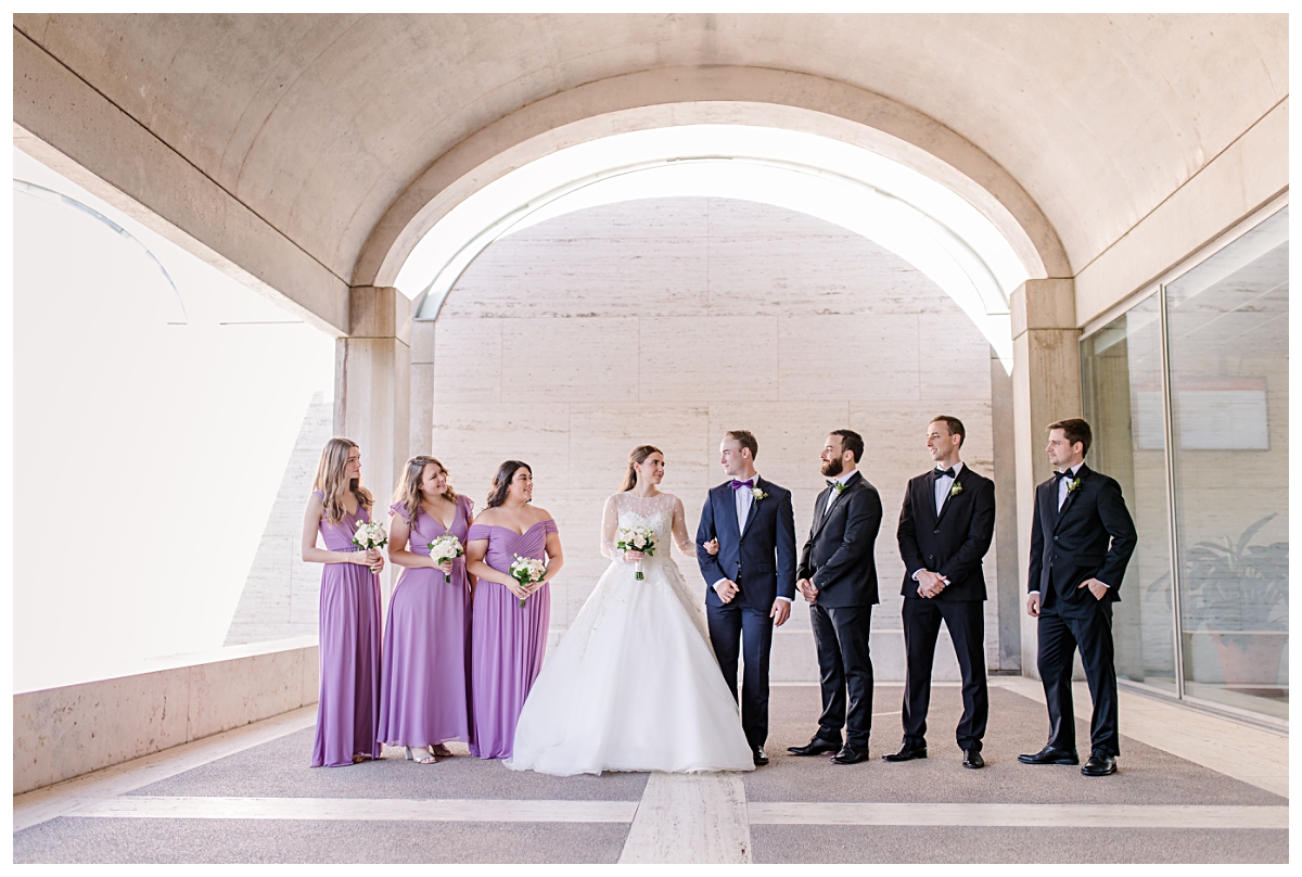 Lilac colored wedding party poses underneath archway for Kimbell Art Museum wedding portraits photographed by Dallas wedding photographer Jenny Bui of Picture Bouquet Studio. 