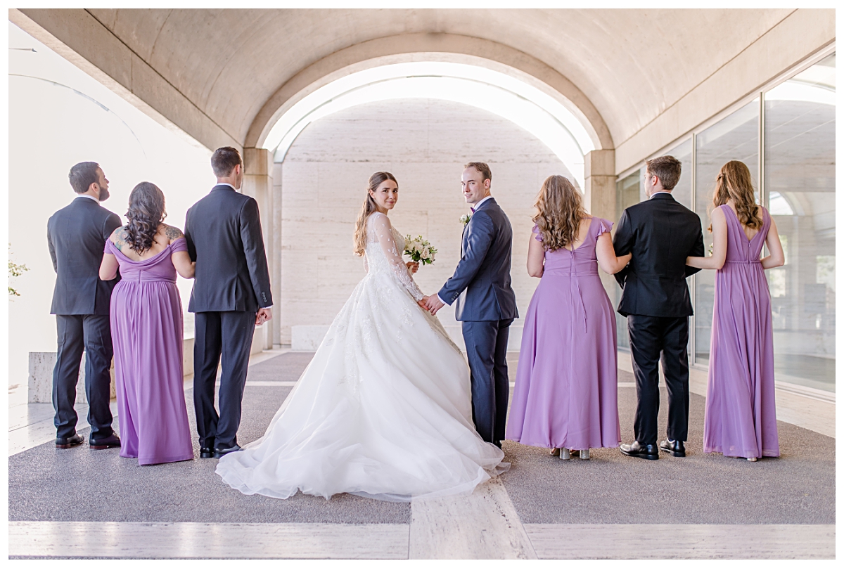 Bride and groom looking back underneath archway at Kimbell Art Museum for wedding day portraits photographed by Jenny Bui of Picture Bouquet Studio. 