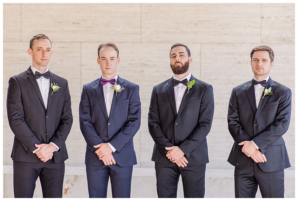 Groomsmen in black suit poses with groom in navy suit at Kimbell Art Museum for wedding day portraits photographed by Jenny Bui of Picture Bouquet Studio. 